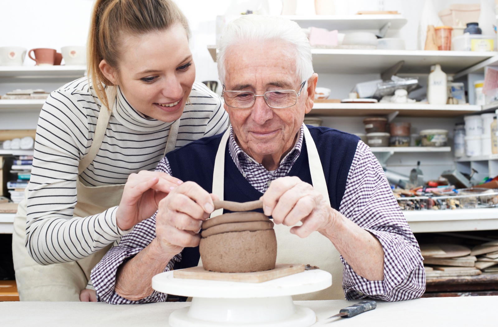 A smiling senior follows the class instructor's directions in a pottery class.
