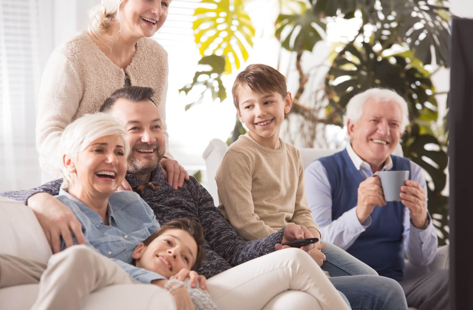 A family enjoying quality time together with their senior grandparents, laughing while crowding together on a couch