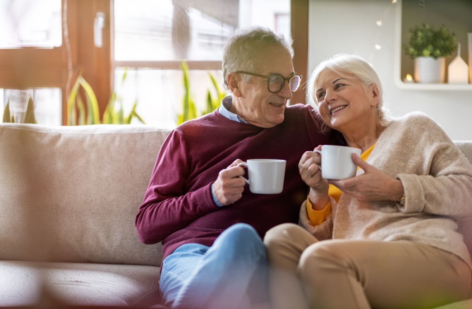 An older adult couple smiling and drinking coffee as they consider retirement communities.