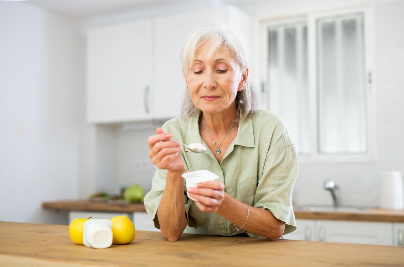 An older adult holding a yogurt container in their left hand with a spoonful of yogurt in their right hand.