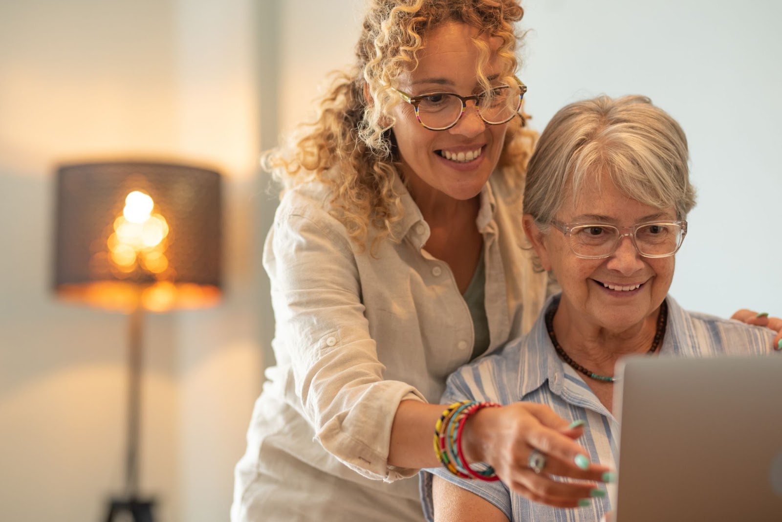 A smiling adult child and her mother researching ways to pay for assisted living on a laptop.