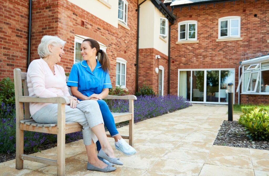 An older adult woman in a senior living facility sitting on a chair smiling and having a conversation with a nurse.