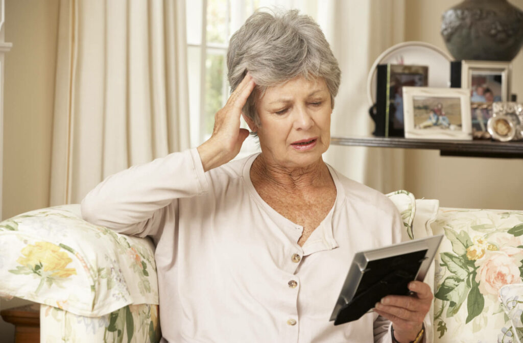  Seated on a couch, an older woman holds her head in her hands and has a look of concentration on her face as she strives to recall the image captured in the photo frame held in her hands.