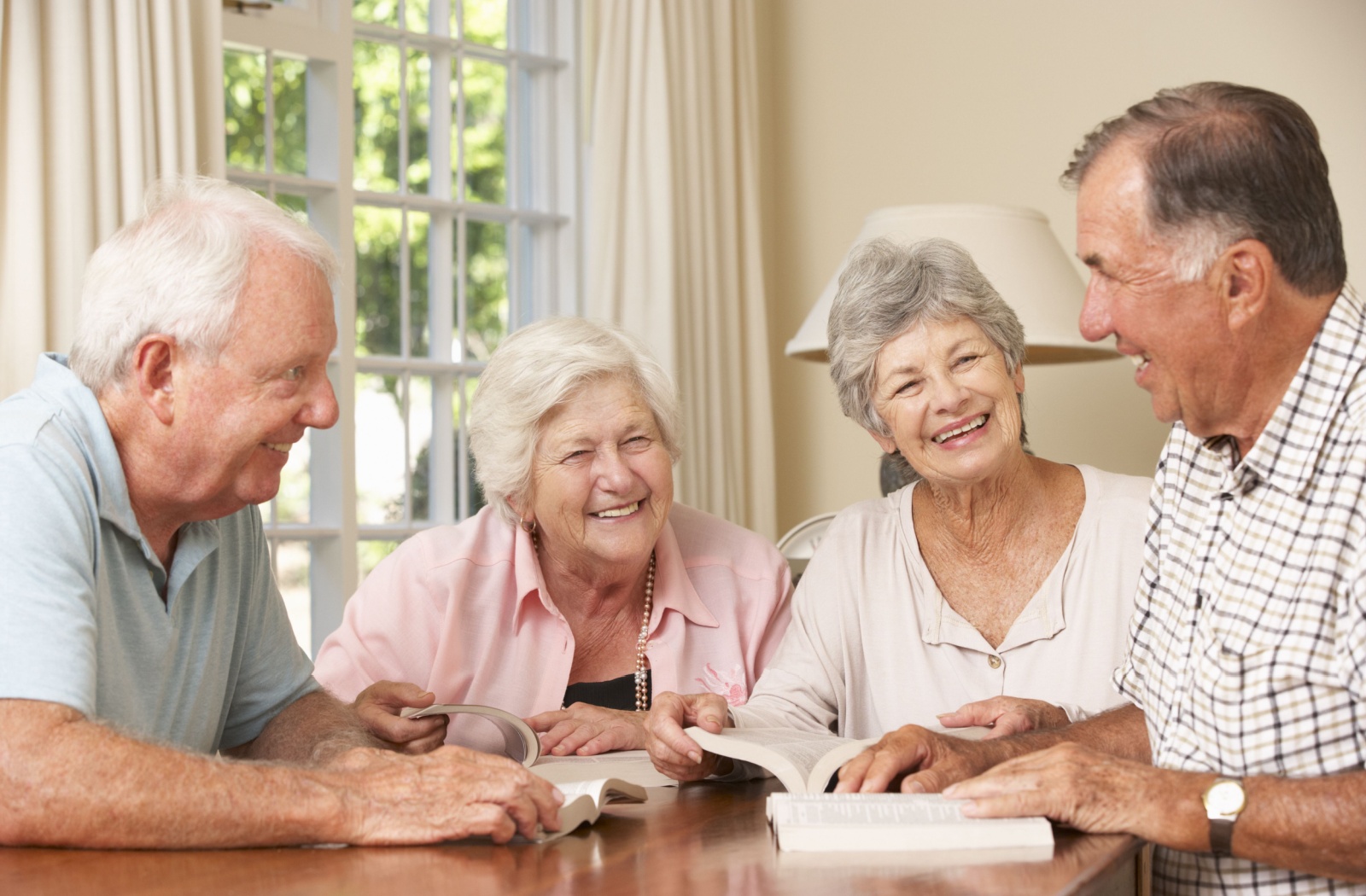 A group of older adults laughing during a book club in their kitchen in senior living.