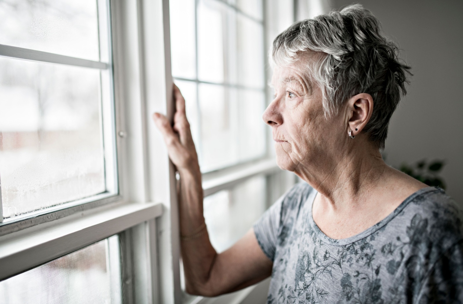 An older adult looking out their window in worry during hurricane season.