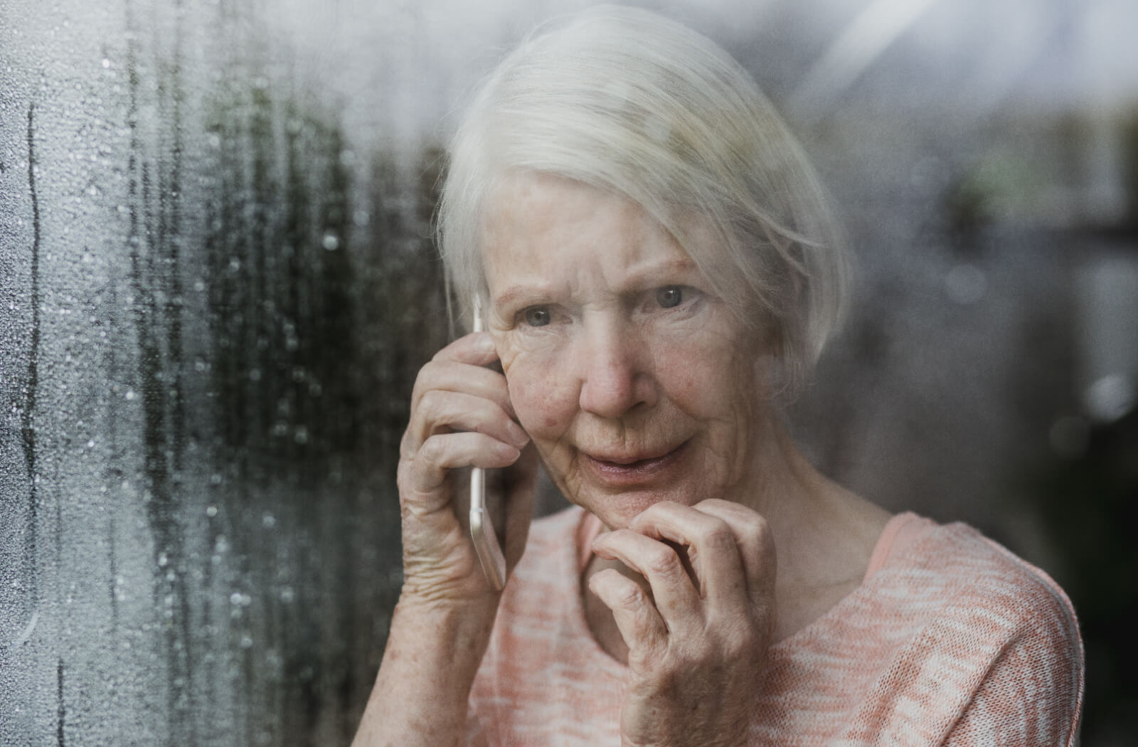An older adult in front of a rain-streaked window calling their loved ones during a hurricane.