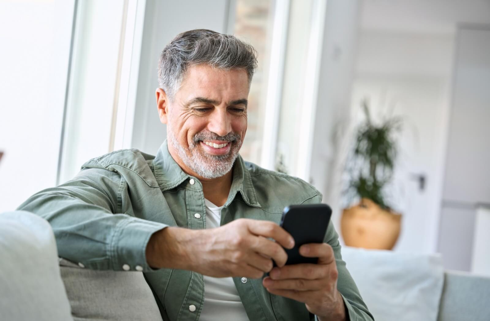A senior smiles while looking at their phone, completing daily word games to help keep their mind sharp