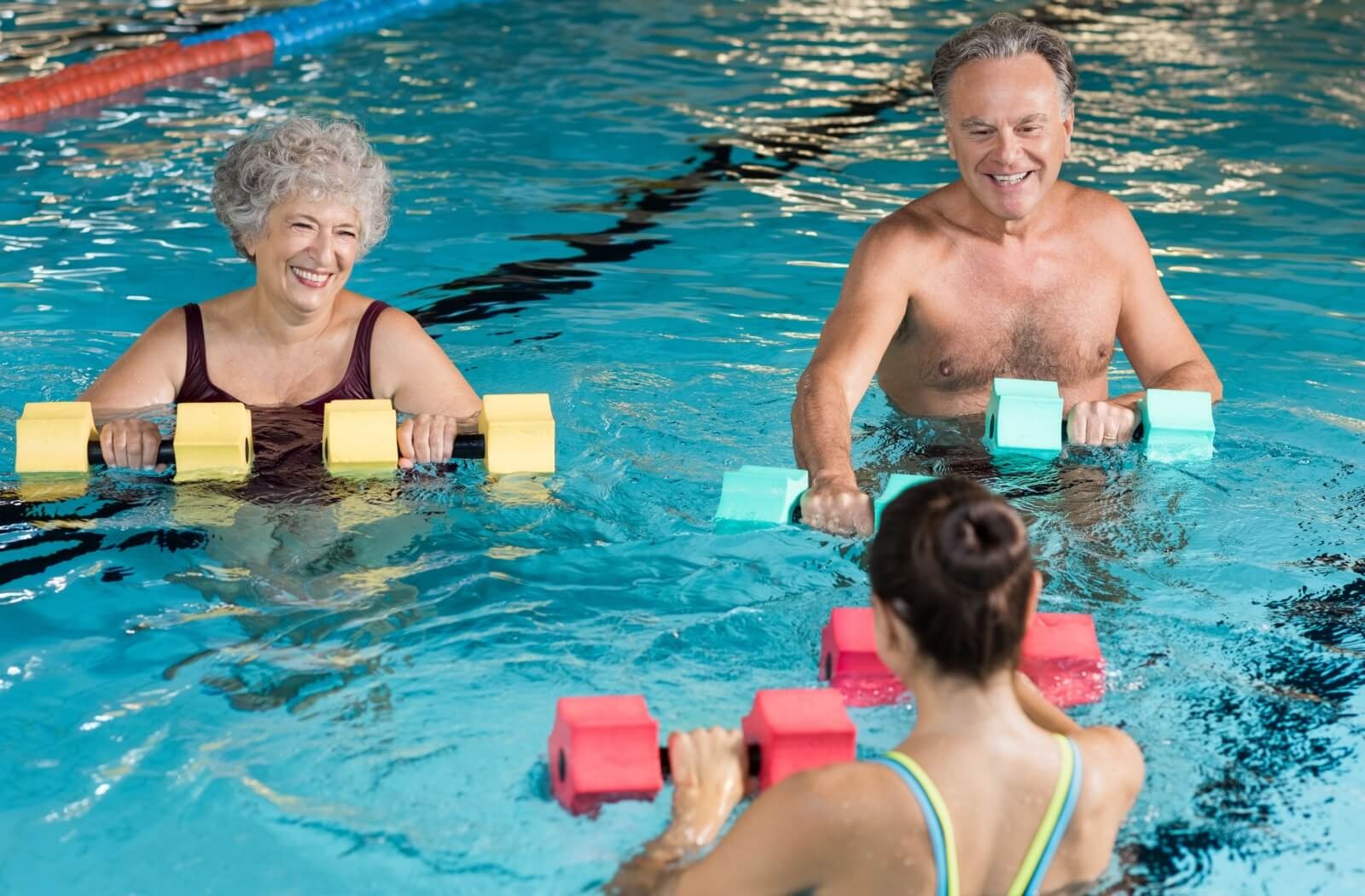 Two older adults participate in a water aerobics class under the guide of an aerobics instructor.